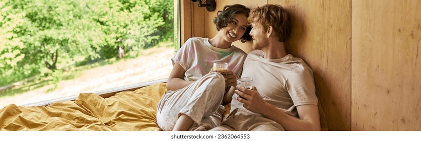 happy interracial couple sitting  on bed and holding cups of morning coffee in country house, banner - Powered by Shutterstock