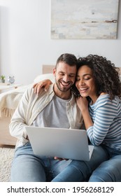 happy interracial couple smiling while looking at laptop