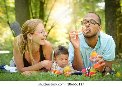 Happy interracial family is blowing bubbles. Happy interracial family is enjoying a day in the park. Mother father and son are smiling and are picnicking in the green park. - Powered by Shutterstock