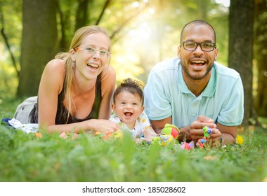 Happy Interracial Family Is Enjoying A Day In The Park. Mother Father And Son Are Smiling And Are Picnicking In The Green Park. Soft Focus Or Shallow Depth Of Field.