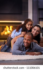 Happy Interracial Family Having Fun At Home By Fireplace, Lying On Each Other's Back, Laughing.