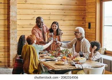 Happy interracial family of three generations toasting by festive table served with homemade food prepared for dinner