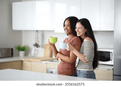 Happy interracial lesbian couple drinking affectionate standing in the kitchen at home - Powered by Shutterstock