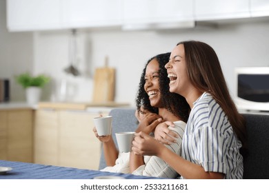 Happy interracial lesbian couple laughing in the kitchen and drinking coffee at home - Powered by Shutterstock