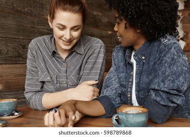 Happy Interracial Lesbian Female Couple Relaxing At Cafe During Lunch: Attractive Woman With Ginger Hair Looking Down And Smiling After Saying Yes To Marriage Proposal Of Her Dark-skinned Girlfriend