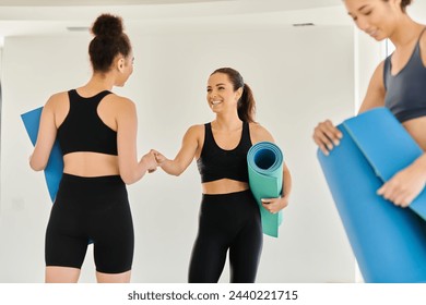 happy interracial women in 20s holding yoga mats and standing together in studio, diversity - Powered by Shutterstock