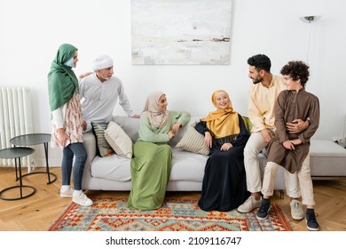 happy interracial women sitting on sofa near muslim family at home