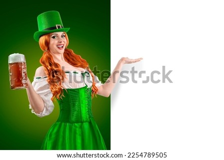 Happy Irish girl holding big mugs with beer or ale. Young red-haired woman аs green Leprechaun elf character for advertising. St. Patrick's Day party. Ireland National Independence Day March 17th.