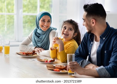 Happy Islamic Family With Little Daughter Eating Tasty Breakfast Together In Kitchen At Home, Joyful Arab Parents And Cute Female Child Enjoying Delicious Food And Drinking Orange Juice, Closeup