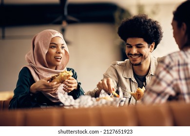 Happy Islamic friends communicating while enjoying on lunch in cafeteria. Focus is on woman in hijab.