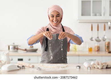 Happy Islamic Lady In Hijab Baking In Kitchen, Sprinkle Flour On Rolled Dough, Smiling Young Muslim Housewife Wearing Apron Preparing Homemade Pastry, Enjoying Cooking At Home, Free Space - Powered by Shutterstock