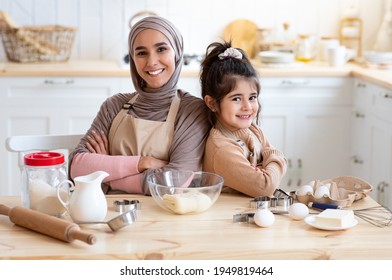 Happy Islamic Mom And Her Little Cute Daughter Posing In Kitchen While Baking Together, Cheerful Muslim Family Enjoying Cooking Homemade Food, Sitting At Table And Smiling At Camera, Free Space - Powered by Shutterstock