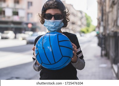 Happy Italian boy wearing a safety mask and sunglasses is going to play with his ball in the street for phase two of the pandemic restrictions due to the COVID-19 coronavirus pandemic.