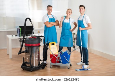 Happy Janitors With Vacuum Cleaner And Cleaning Equipments In Office