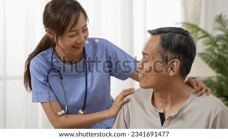 happy Japanese senior man having pleasant talk with friendly personal care attendant at home. the woman putting hands on his shoulders showing support
