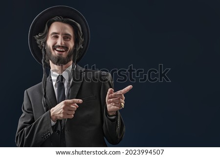 Happy Jew laughs and points his fingers to the side. Studio shot on a dark blue background. 