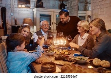 Feliz familia extendida judía celebrando Hanukkah y tostando durante la cena en la mesa.