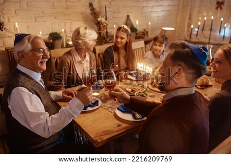 Happy Jewish family celebrating Hanukkah while having dinner together at dining table. Focus is on men toasting with Kosher wine. 