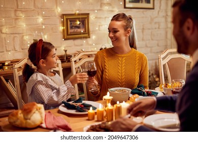 Happy Jewish Family Eating Lunch At Dining Table During Hanukkah. Focus Is On Mother And Daughter Toasting With Each Other.