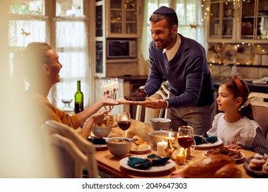 Happy Jewish Family Having Traditional Hanukkah Meal At Dining Table. Focus Is On Father Serving Beef Brisket.