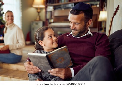 Happy Jewish Father And Daughter Talking While Reading Hebrew Bible During Hanukkah At Home.