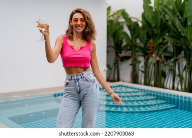 Happy Joiful Woman In Colorful Summer Outfit Holding Glass Of Wine, Posing Near Pool On Luxury Villa. Party Mood.