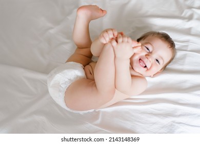 happy joyful baby in diapers lying on white bed