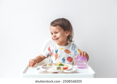 happy joyful baby girl 1.5 years old sitting in a high chair on a white background, eating, showing tongue, looking at the camera, concept of baby food and complementary feeding. - Powered by Shutterstock