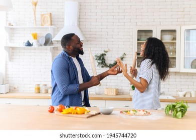 Happy Joyful Black Couple Husband And Wife Having Fun Singing In The Kitchen, Cooking Together At Home. Overjoyed Young Couple In Love Preparing Meal Healthy Food, Enjoying Active Family Weekend