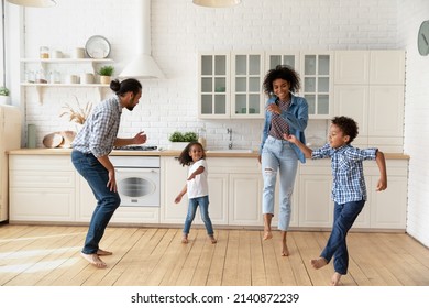 Happy Joyful Black Couple And Sibling Kids Dancing Rock-n-roll In Kitchen. Active Parents And Energetics Children Celebrating Family Event, Having Fun To Music, Enjoying Party, Exercising