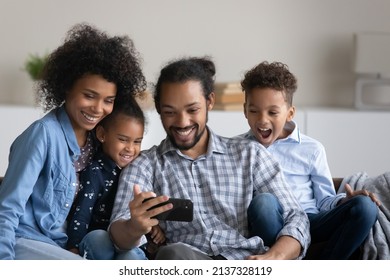 Happy joyful Black family with beloved preschool kids taking selfie on smartphone. Young couple of parents and siblings resting on couch, posing for self portrait on cellphone, having fun, laughing - Shutterstock ID 2137328119
