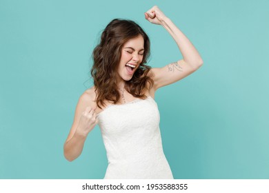 Happy joyful bride young woman in white wedding dress doing winner gesture celebrating clenching fist say yes isolated on blue turquoise background studio portrait. Ceremony celebration party concept