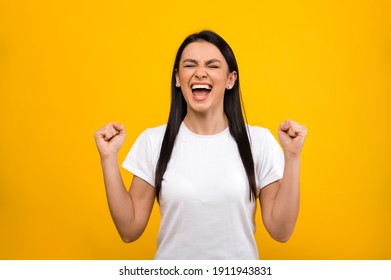 Happy joyful caucasian girl wearing basic white t-shirt, rejoicing in success or winning, standing on orange isolated background - Shutterstock ID 1911943831