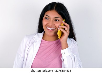 Happy Joyful Charming Young Hispanic Doctor Girl Wearing Coat Over White Background Talk Speak Phone Smile Good Mood