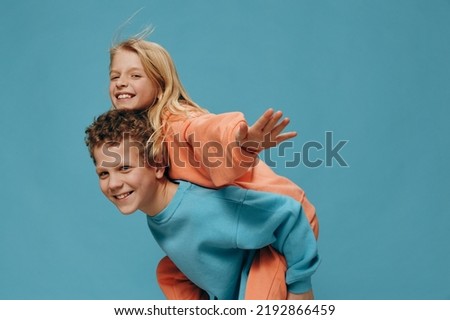 happy joyful children, brother and sister of school age play together and the boy rolls the girl on his back. Horizontal studio photography on a blue background