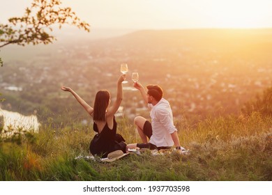 Happy joyful couple with hands up enjoy view and beautiful sunset at summer picnic. View from back.