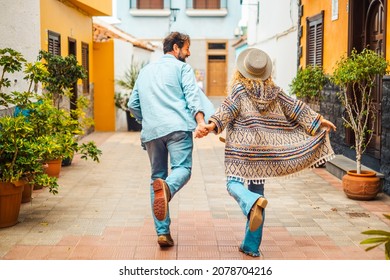 Happy and joyful couple running on the street in the touristic city. Concept of happiness and overjoyed man and woman viewed from back walking holding hands together - Powered by Shutterstock