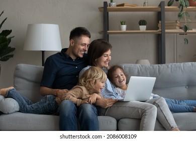 Happy Joyful Family Watching Online Movie On Laptop, Relaxing On Sofa Together, Enjoying Internet TV Channel, Making Video Call. Millennial Parents And Two Children Resting At Home