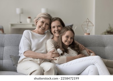 Happy joyful girls and women of three family generations relaxing on home sofa together, hugging, cuddling kid, looking at camera, laughing, smiling, enjoying leisure time, weekend - Powered by Shutterstock