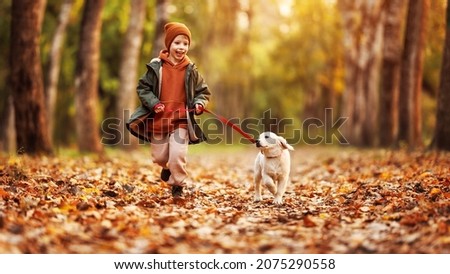 Happy joyful little boy walking with his buddy golden retriever puppy in beautiful autumn forest, child playing and having fun with dog during walk in nature. Children and pets outdoors
