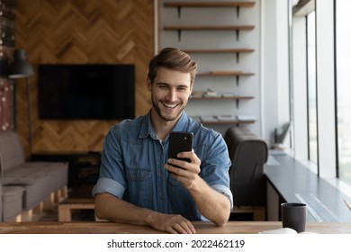 Happy joyful millennial handsome guy taking picture on smartphone, using online app on gadget. Young man making video call from home, talking via virtual conference chat, smiling at cellphone camera