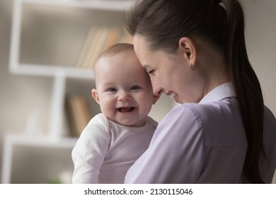 Happy Joyful Mother Holding Cute Funny Baby In Arms, Hugging Child With Face Touches, Laughing, Having Fun. Infant Kid Looking At Camera, Smiling With Open Toothless Mouth