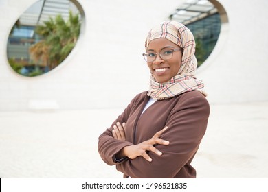 Happy Joyful Muslim Businesswoman Posing Outside. Young Dark Skinned Business Woman In Hijab And Office Suit Standing For Camera With Arms Folded And Smiling. Business Lady In Hijab Concept