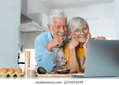 Happy joyful older husband and wife sharing cooking looking laptop, making organic fresh salad together, following recipe, talking, laughing. Old couple having fun in kitchen, preparing dinner - Powered by Shutterstock