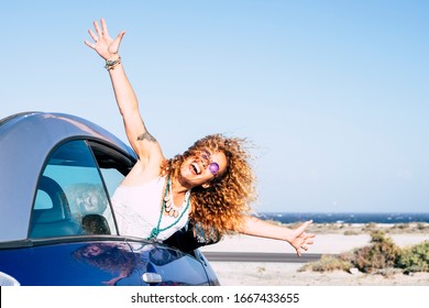 Happy and joyful people in outdoor travel leisure activity - beautiful curly blonde woman have fun outside the window of a blue vehicle car - concept of transport and happiness - ocean background - Powered by Shutterstock