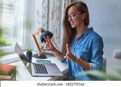 Happy joyful smiling casual woman learning and communicates in sign language online at a laptop at cozy comfy home by the window