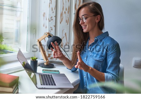 Happy joyful smiling casual woman learning and communicates in sign language online at a laptop at cozy comfy home by the window 