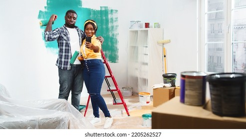 Happy joyful young African American cute couple hugging posing to smartphone camera taking selfie photos and smiling while standing in room during home repair, renovation improvement - Powered by Shutterstock