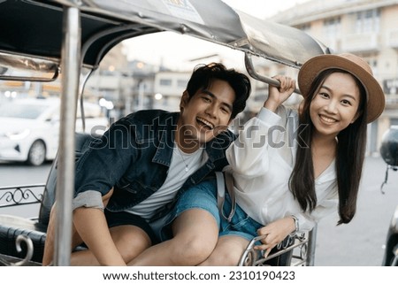 Happy and joyful Young Asian couple traveler tourists riding a tuk tuk tour, rickshaw style transportation on the street in Bangkok in Thailand - people traveling enjoying local culture concept