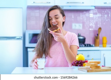 Happy Joyful Young Breakfast Woman Eating Toast Bread With Nut Chocolate Cream For A Dessert At Home 